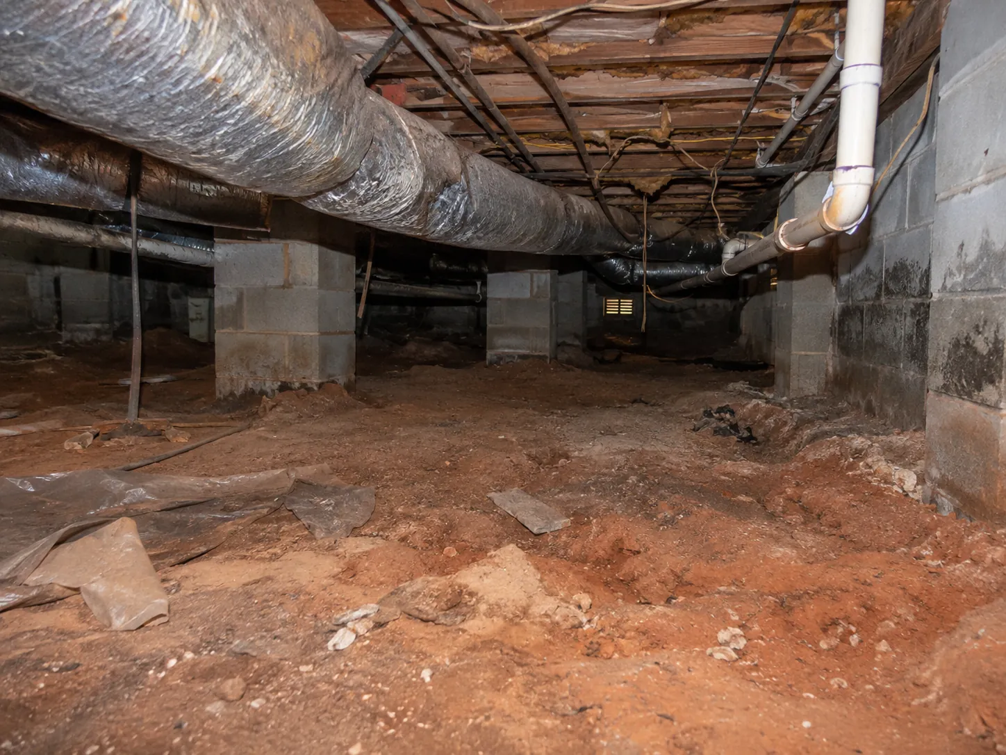 A bare crawl space floor with exposed soil before a vapor barrier is installed
