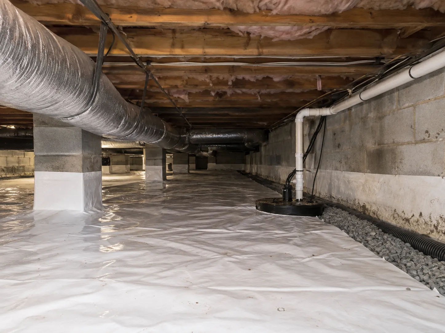 A sealed crawl space floor with a sump pump basin and drainage system after waterproofing