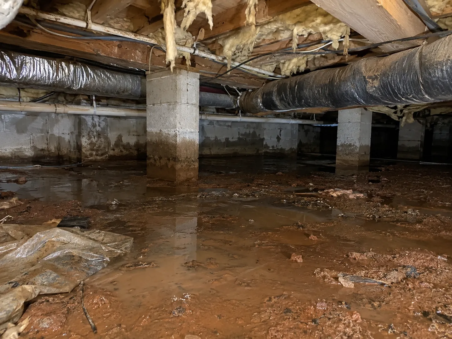 Standing water and mud on a crawl space floor after heavy rain