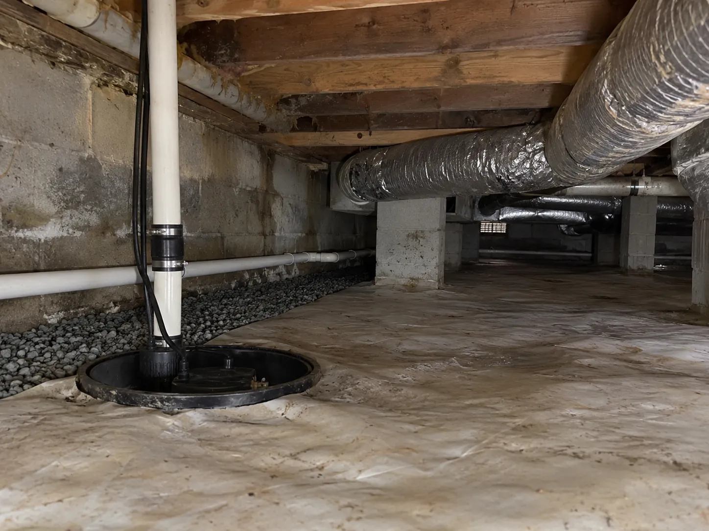 An interior drainage channel with gravel and a sump pump basin installed along a crawl space wall